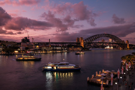 Circular Quay, Sydney, Australia - 6th December 2022: Sun setting over Sydney Harbour Bridge as ferries arrive and depart from Circular Quayのeditorial素材
