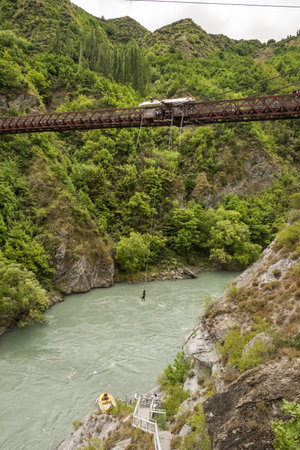 Kawarau Bridge, Queenstown, New Zealand - 20th December 2022: A bungy jumper hangs above the Kawarau River near Queenstown in New Zealand after jumping from the Kawarau Bridge, the birthplace of bungy jumpingのeditorial素材