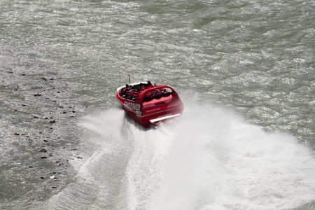 Shotover River, Queenstown, New Zealand - 20th December 2022: A Shotover Jetboat full of passengers skims over the shallow rocky waters of the Shotover River near Queenstown in New Zealandのeditorial素材
