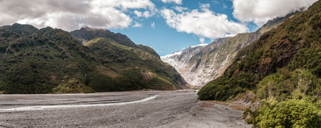 Panoramic view of the alluvial bed of the Waiho River flowing from the Franz Josef Glacier and snow capped mountains in New Zealandの写真素材
