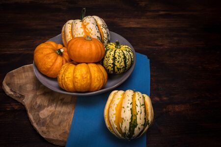 Assortment of decorative and edible pumpkins and gourds in grey ceramic bowl on vintage wooden background with blue cloth.の写真素材