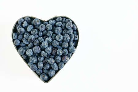 Blueberries in heart shaped bowl on white background. Copy space to rightの写真素材