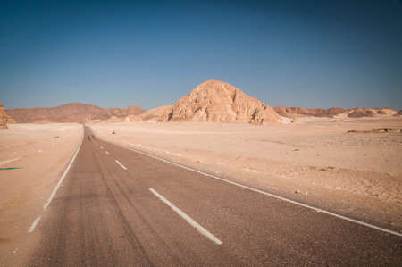 Desert landscape with blue sky and sun with road,sand and mountains