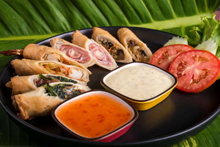 black plate with a fusion of spring rolls dispalyed with dipping sweet chilli sauceand mayonaiseの写真素材