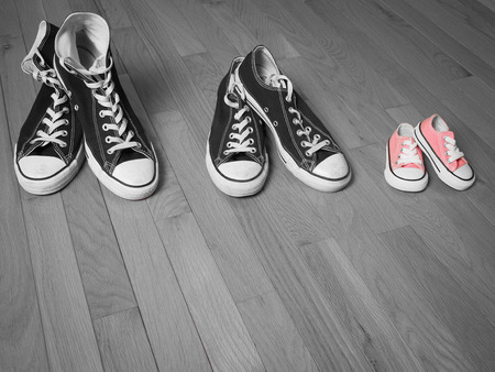 An image of two pairs of adults sneakers in black and white next to a baby pair of sneakers in pinkの写真素材