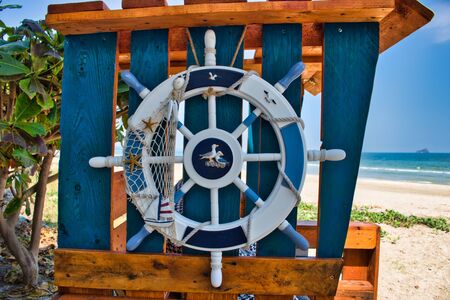This unique photo shows a beach chair on the beach on which a wooden steering wheel is beautifully decorated with seagullsの写真素材