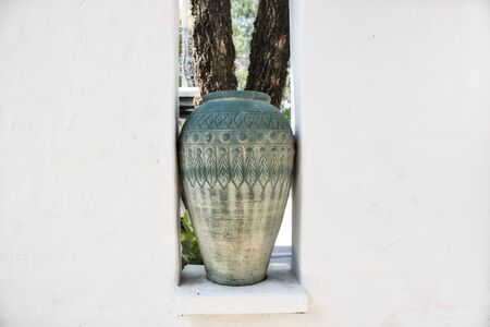 This unique photo shows a large clay vase in green standing between a white wall. It looks very decorative...の写真素材