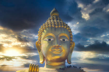 This unique photo shows the golden head of a large Buddha statue and a dreamy sunset with red clouds in the sky of Hua Hin in Thailand.の写真素材