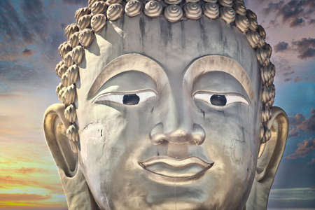 This unique photo shows the golden head of a large Buddha statue and a dreamy sunset with red clouds in the sky of Hua Hin in Thailand.の写真素材