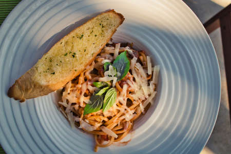 This unique photo shows the Italian meal spaghetti bolognese. Served in a deep plate with garlic baguette and a basil leaf as decoration.の写真素材