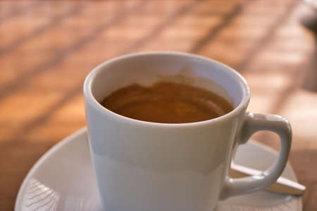 This unique photo shows a white cup with a saucer and inside it a hot cafe with a cream on top. The picture was taken from the sideの写真素材