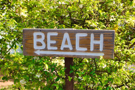 This unique photo shows a wooden sign in nature on which Beach is written and an arrow to the leftの写真素材