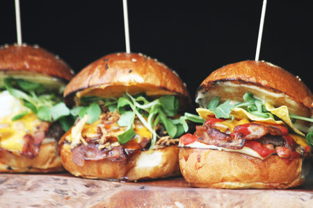 Three artisanal burgers with rich toppings presented on rustic wood, highlighted by soft lighting