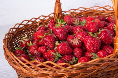 Wicker basket filled with ripe strawberries. On a white wooden background. Photo.