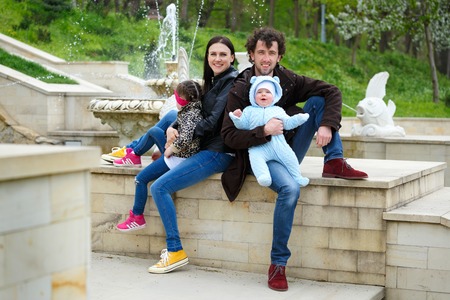 Family life. Parents and their children sit on background of fountain. Girl was offended and turned away. Horizontally framed shot.の写真素材