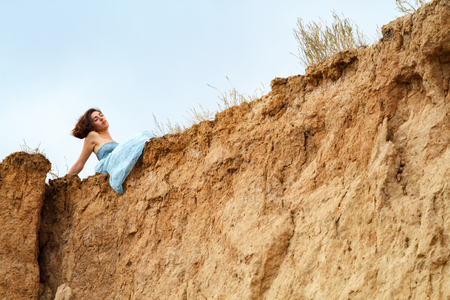 Beautiful mountains of orange clay against the blue sky. The girl in a blue dress is sitting at the top of the mountain. Space for text. Horizontally framed shot.の写真素材