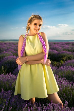A young, pretty blonde with long pink braids stands in a lavender field. Vertically framed shot.の写真素材