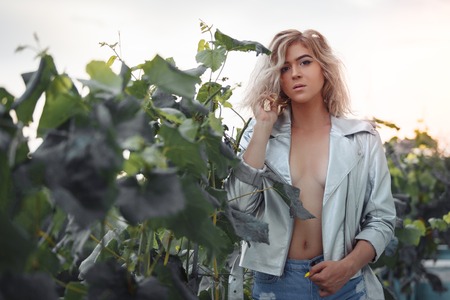 Young slim model in sexy clothes posing in grape bushes. Horizontally framed shot.