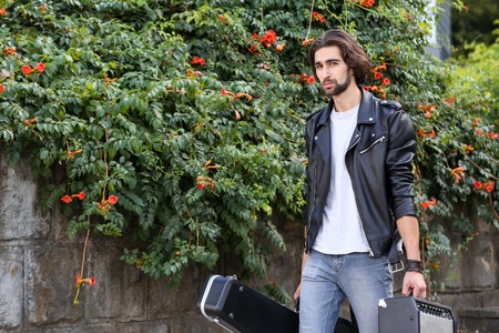 Street musician holding a case with a guitar and amplifier. Vagrant lifestyle. Playing to make money...