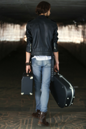 Street musician holding a case with a guitar and amplifier. Rear view. A blurry picture. Vagrant lifestyle. Playing to make money a living. Unemployed musician. Future rock star. Vertically framed shot.の写真素材