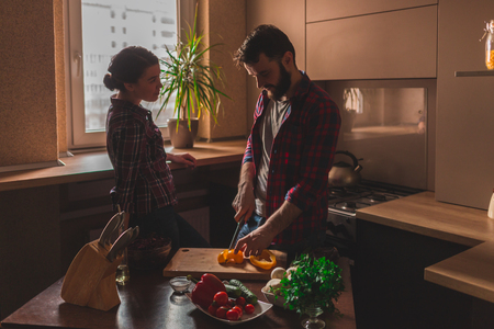 Beautiful young couple in kitchen at home while cooking healthy food. Man cuts a pepper. Woman looks at her husband.の写真素材