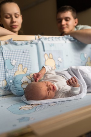 Woman and man look at newborn. Boy sleeps in his crib.