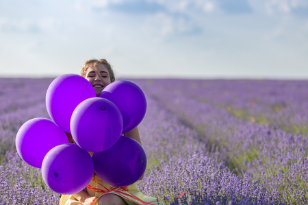 Portrait of a happy and joyful girl in yellow dress with a balloons in her hands. In the background, a lavender field and blue sky. Horizontally framed shot.の写真素材