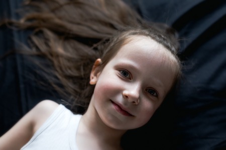 A portrait of a little girl lying on a black sheet. Horizontally framed shot.の写真素材