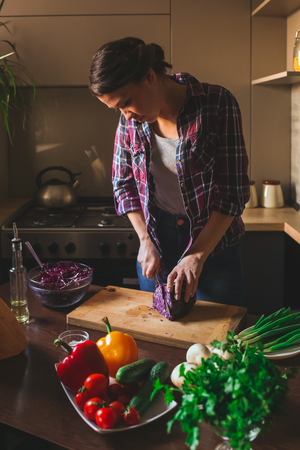 Beautiful brunette working in the kitchen. Woman cuts vegetables.の写真素材