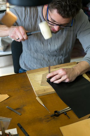 Leather craftsman working with natural leather using hammer. Handmade concept. Concept of small...