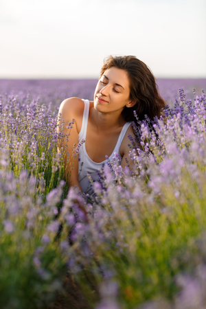Portrait of a beautiful brunette in a lavender field. She closed her eyes in pleasure. Horizontally framed shot.の写真素材