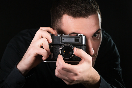 Man photographer holding a retro photo camera. Shooting process. Photographer looks at viewfinder. Horizontally framed shot.の写真素材