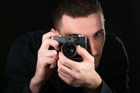 Man photographer holding a retro photo camera. Shooting process. Photographer looks at viewfinder. Horizontally framed shot.の写真素材