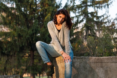 Sexy brunette sits in a defiant pose. Green firs in background. Horizontally framed shot.の写真素材