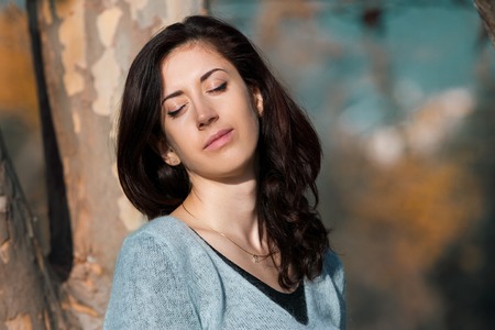Portrait of a beautiful young woman with her eyes closed against a tree and autumn yellow foliage....