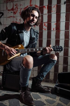 Street musician sitting on the amplifier and playing guitar in the underpass.の写真素材