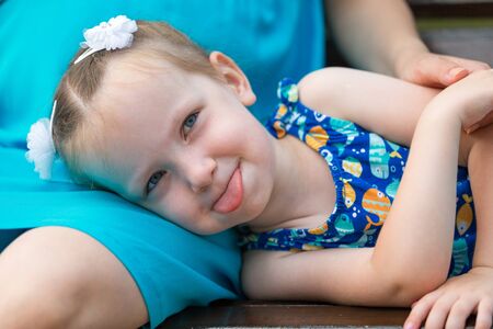 A little girl lies on her mother's lap and shows her tongue. Horizontally framed shot.の写真素材