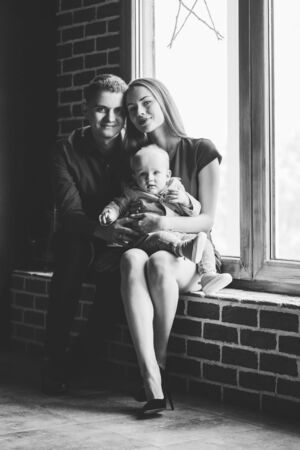Parents and their child sitting at the window. Mom, dad and baby. Portrait of young family. Happy family life. Man was born. Vertically framed shot.の写真素材