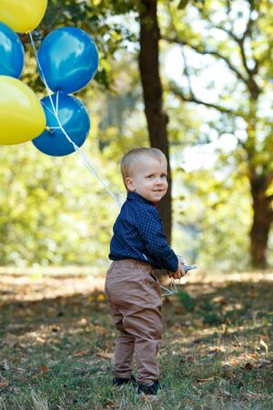 Portrait of a cute little boy on the background of nature. He's holding balloons. Walk in park. Family life. Vertically framed shot.の写真素材