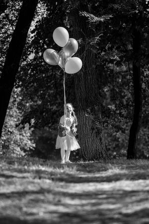 Little cute girl running in the Park with a bunch of balloons. She laughs provocatively. The concept of a happy childhood. Vertically framed shot.の写真素材