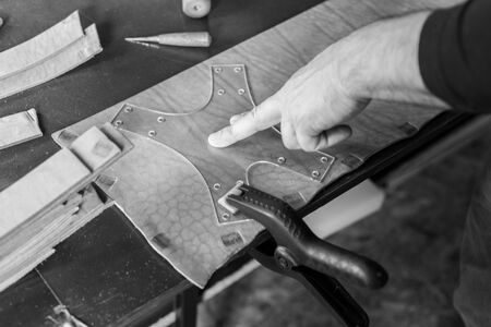 The master working with leather. On brown wooden table scattered with tools and accessories. Horizontally framed shot.の写真素材