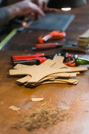 The master working with leather. On brown wooden table scattered with tools and accessories. Horizontally framed shot.の写真素材