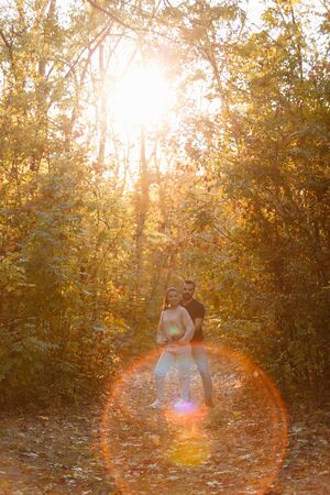 Young couple in love hugging in the Park. Man and woman alone with each other. Warm autumn evening in forest. Rays of the setting sun break through the branches of the trees. Vertically framed shot.の写真素材