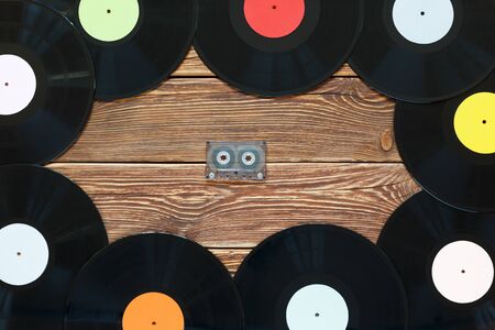 One vintage cassette tape and vinyl records on a wood table background. Multicolored labels. Top view. Place to copy space. Horizontally framed shot.の写真素材