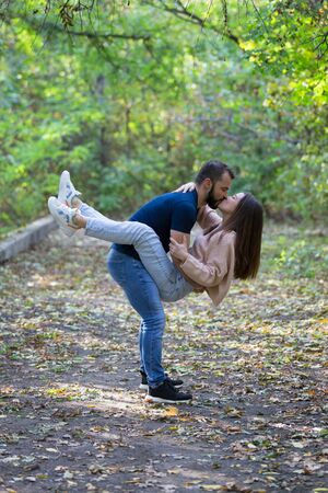 Young beautiful couple in the Park. A man holds a woman in his arms. In the background autumn forest. Vertically framed shot.の写真素材