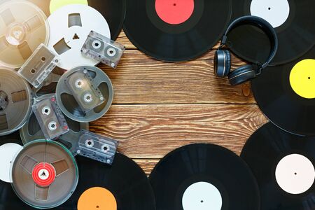 Old vintage bobbins, vinyl records, cassette tapes and headphones on a wood table background. Multicolored labels. Top view. Place to copy space. Sun glare. Horizontally framed shot.の写真素材