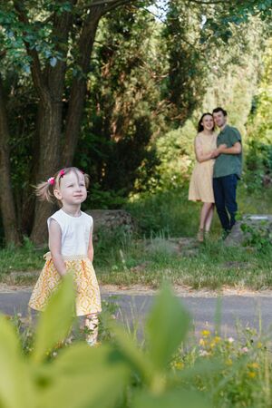 In foreground walking girl. In background parents embracing each other looking at her. Vertically framed shot.の写真素材