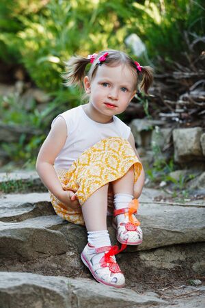 Portrait of a cute little girl on the background of nature. She's sitting on the rocks. Vertically framed shot.の写真素材