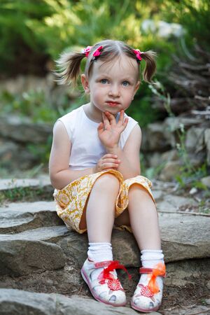 Portrait of a cute little girl on the background of nature. She's sitting on the rocks. Vertically framed shot.の写真素材