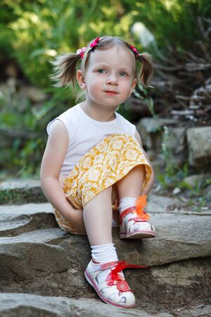 Portrait of a cute little girl on the background of nature. She's sitting on the rocks. Vertically framed shot.の写真素材